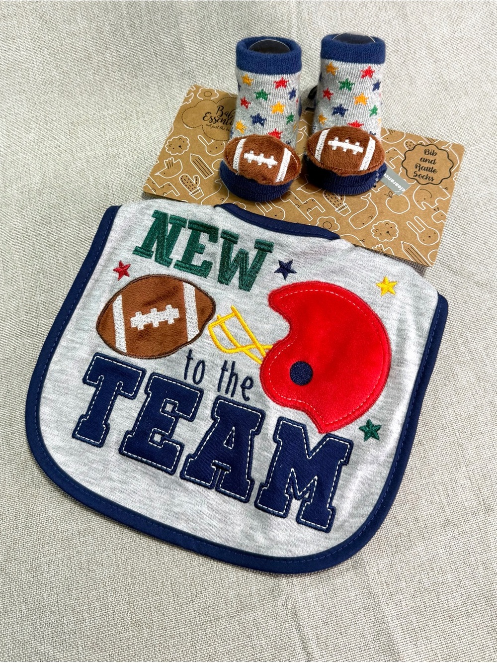 Baby Essentials 2-piece set ‘New to the Team' Grey Bib and matching rattle socks